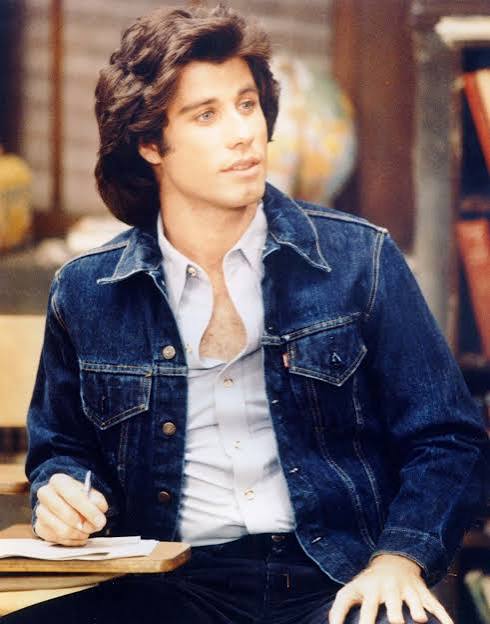 TV still of a young man at a classroom desk in a denim jacket, holding a pen