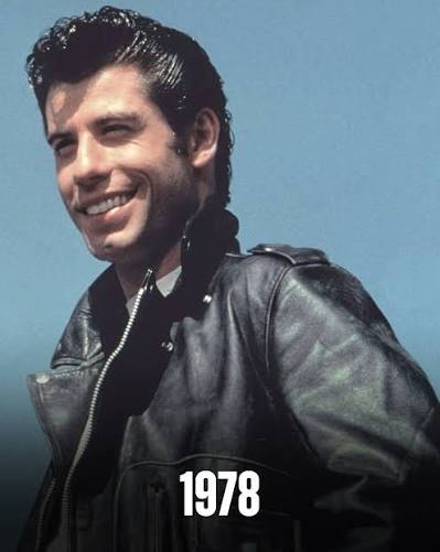 Promotional photo from Grease of a man with slicked-back hair smiling against a blue sky